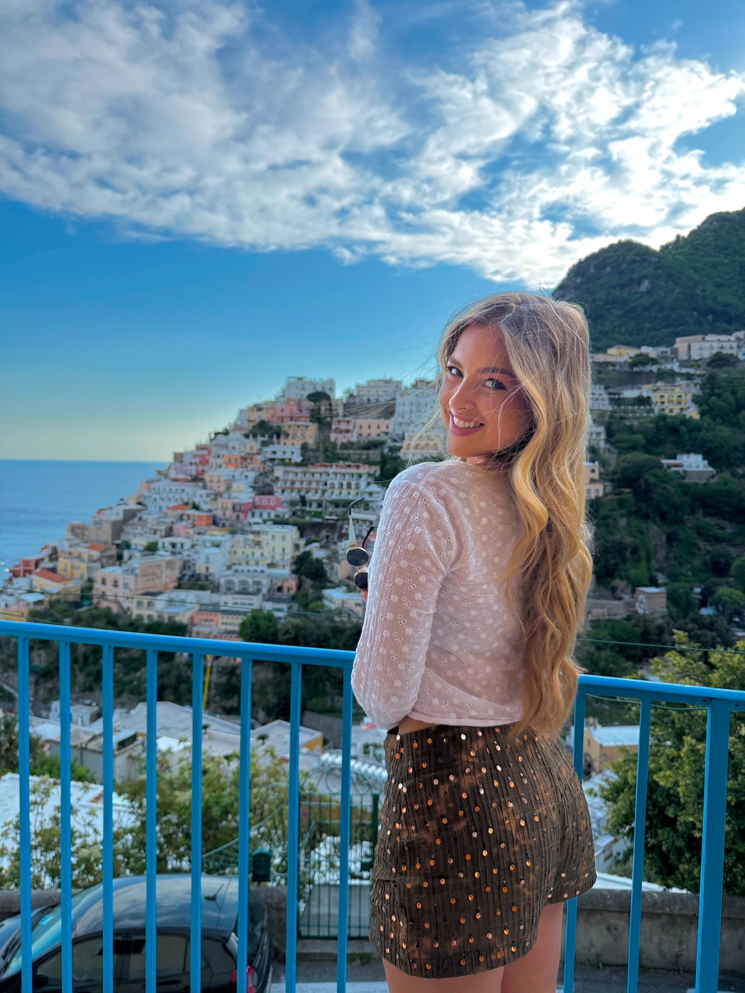 Kaylyn Camille smiling on a balcony overlooking a coastal town